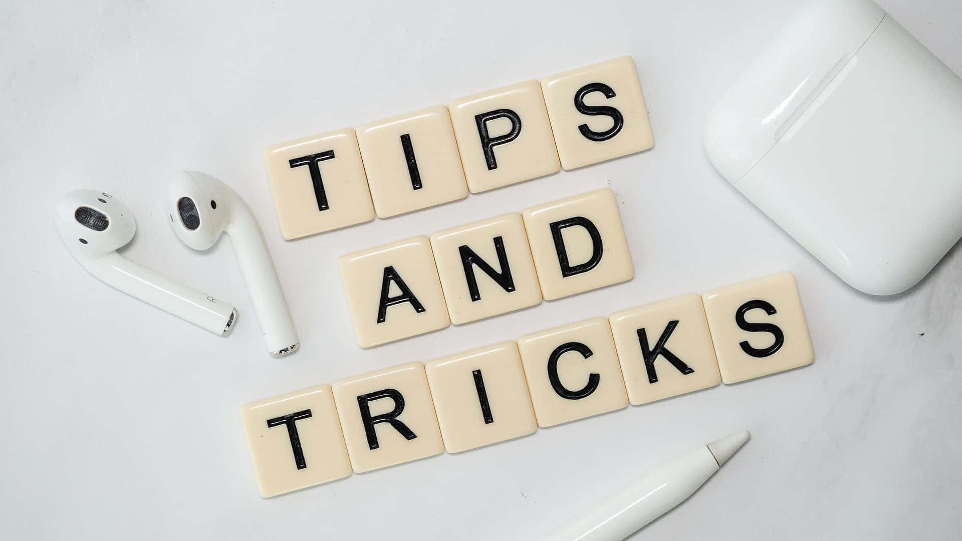Brickor med bokstäver som bildar ordet Tips and tricks. I bilden även ett par air pods och en penna.